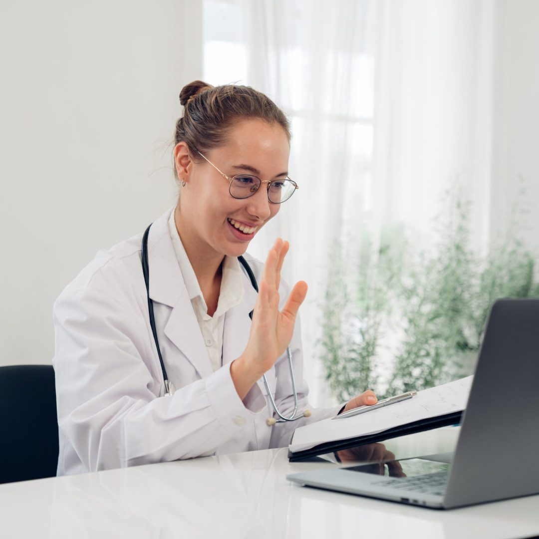 Female doctor in uniform greeting patients online on laptop during on line meeting.